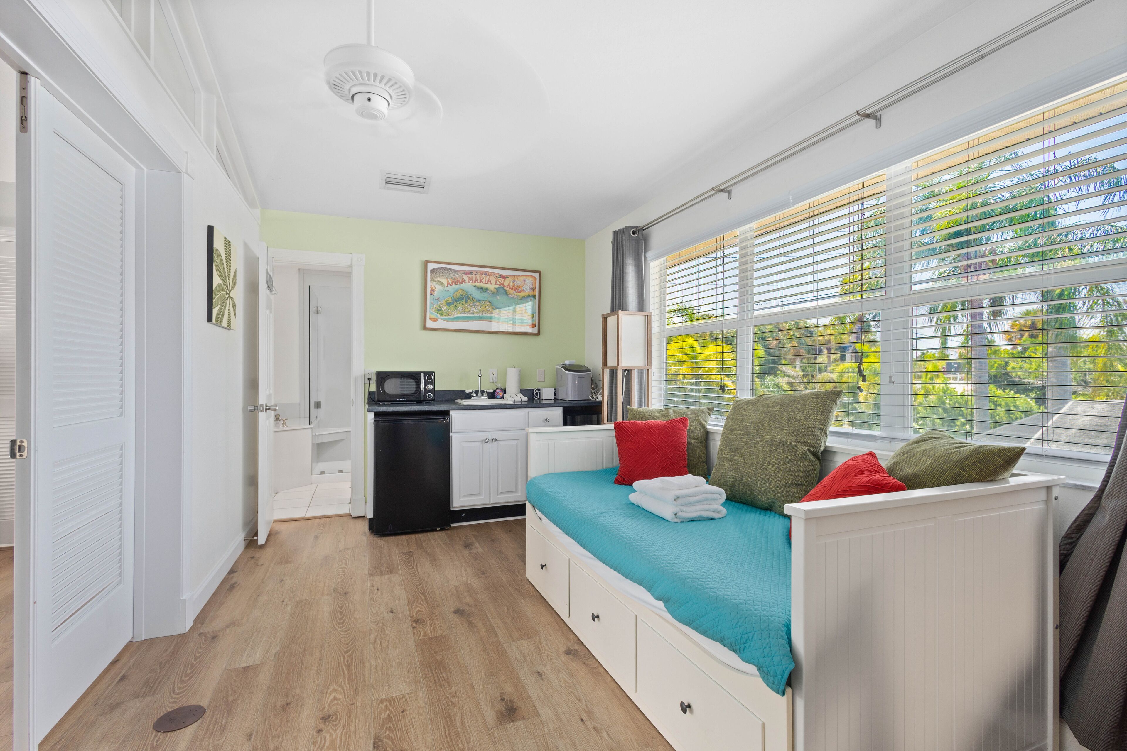 A compact room with a bed, kitchenette, and a window with blinds.