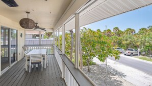 A covered outdoor area with a table and chairs, a ceiling fan, and a view of a road with palm trees. - AMI Du Soleil | 1 Block 2 Beach, Big Heated & Shaded Saltwater Pool, Lanai, Grill, Walk to Restaurants, Cafes, Shops, Bars (Anna Maria)