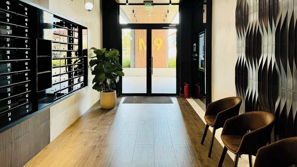 Een hotel lobby met een receptiebalie, een grote potplant, een brandblusser en een muur met een geometrisch patroon.