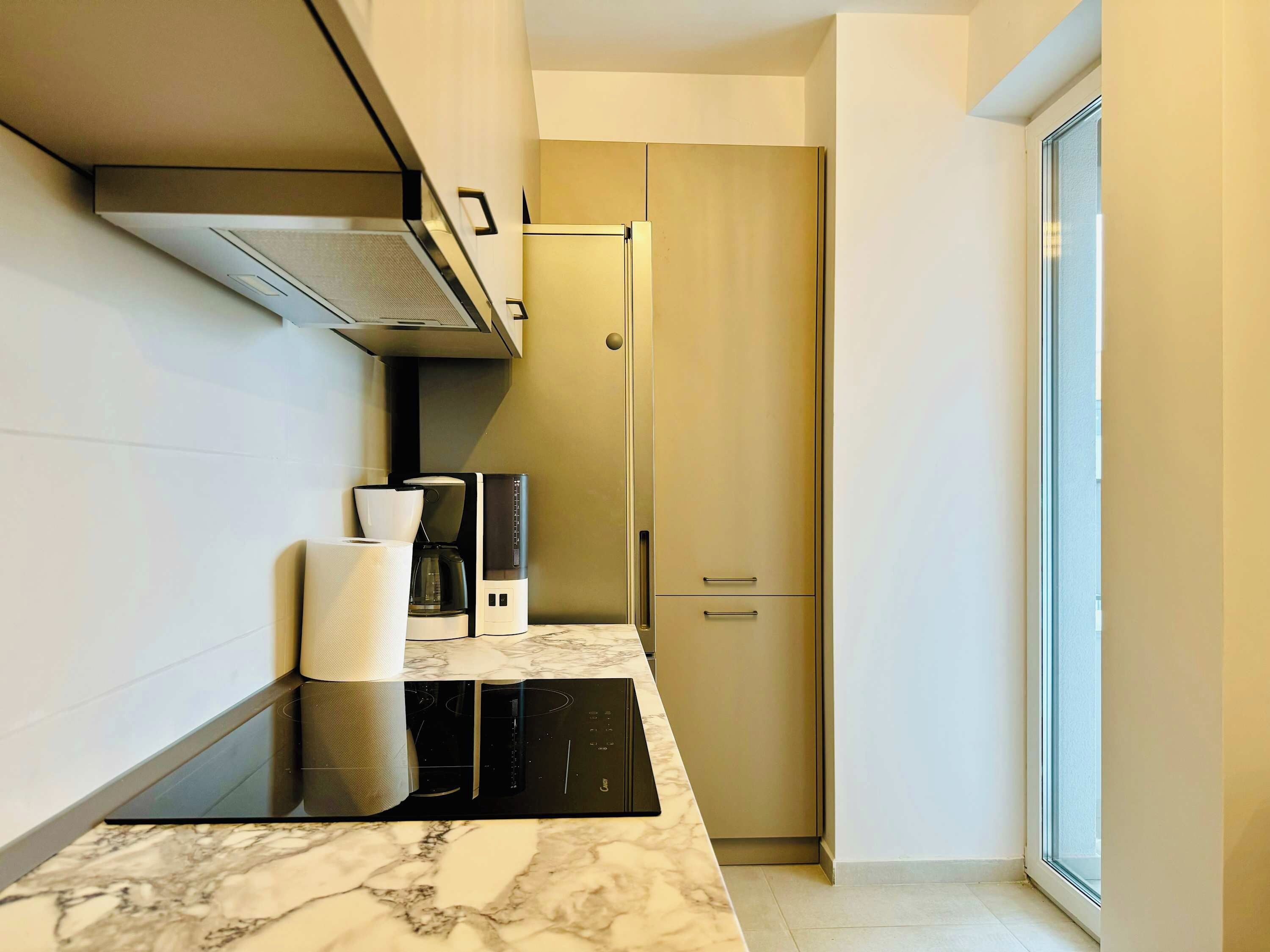 A modern kitchen with a built-in stove, a coffee maker, and a refrigerator.
