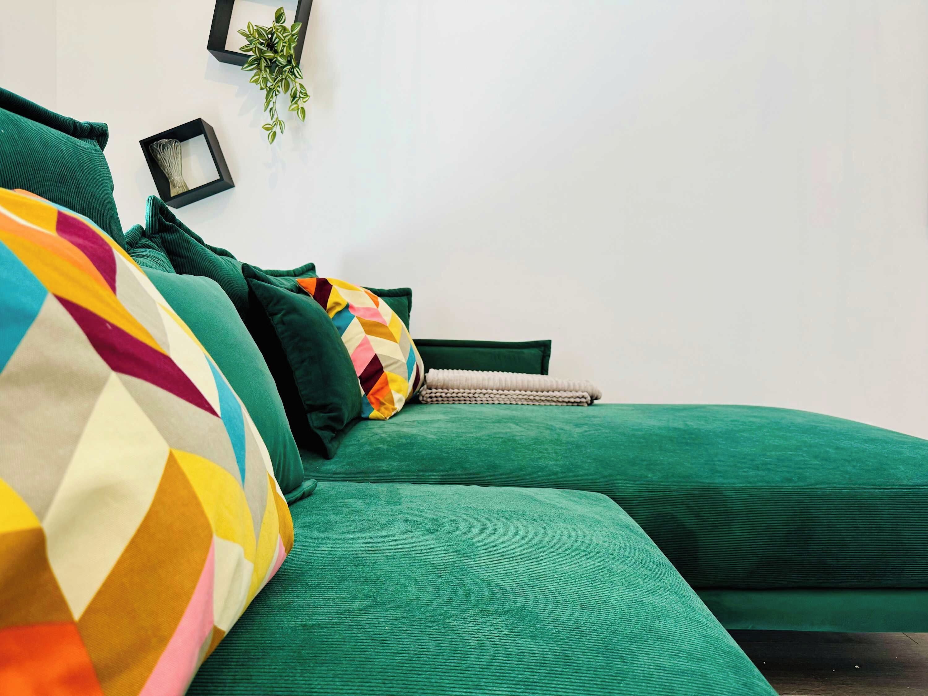 Um sofá estofado verde com almofadas coloridas e um cobertor branco.