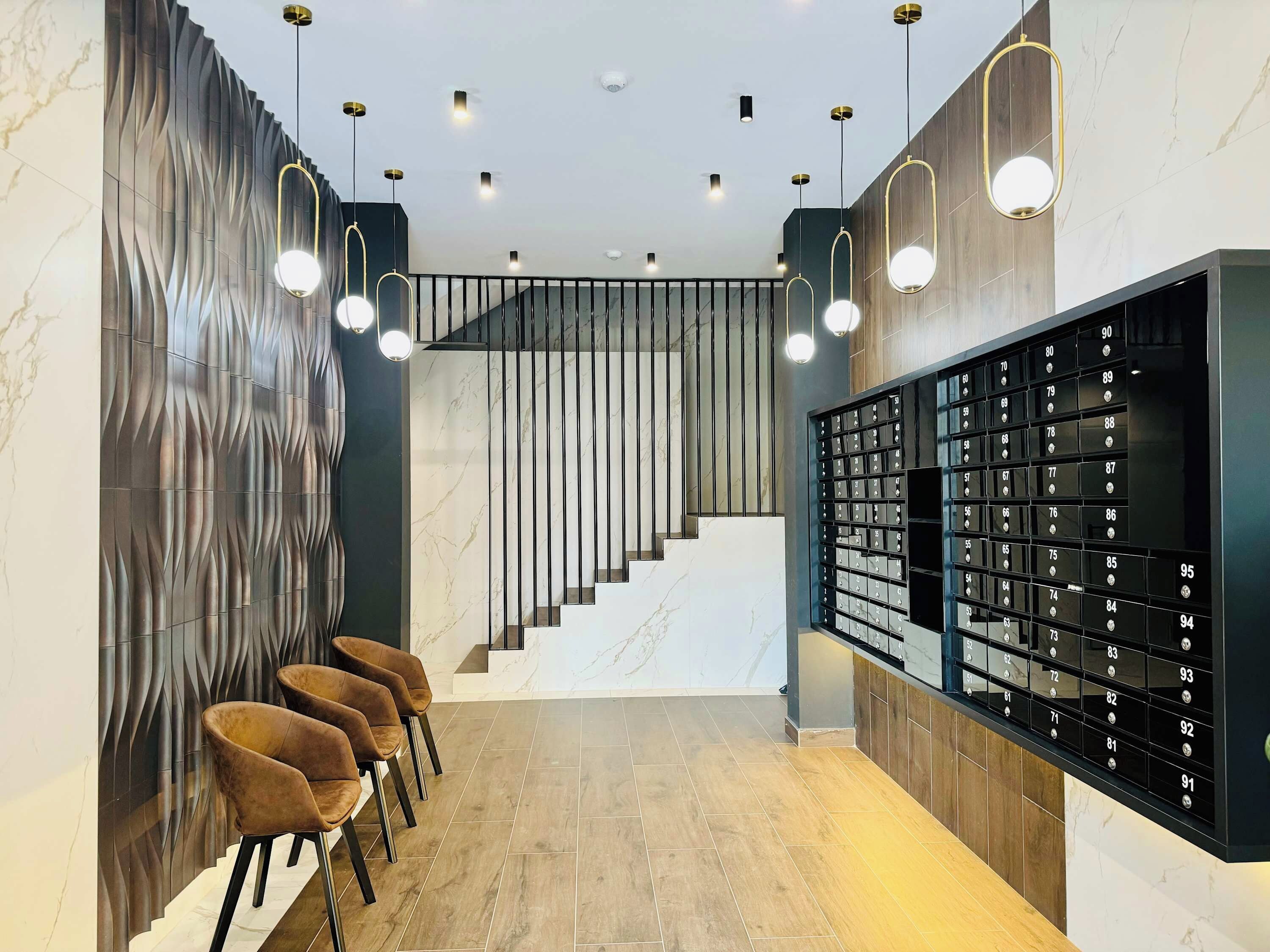 A modern lobby with a marble staircase, a row of chairs, and a wall of numbered lockers.