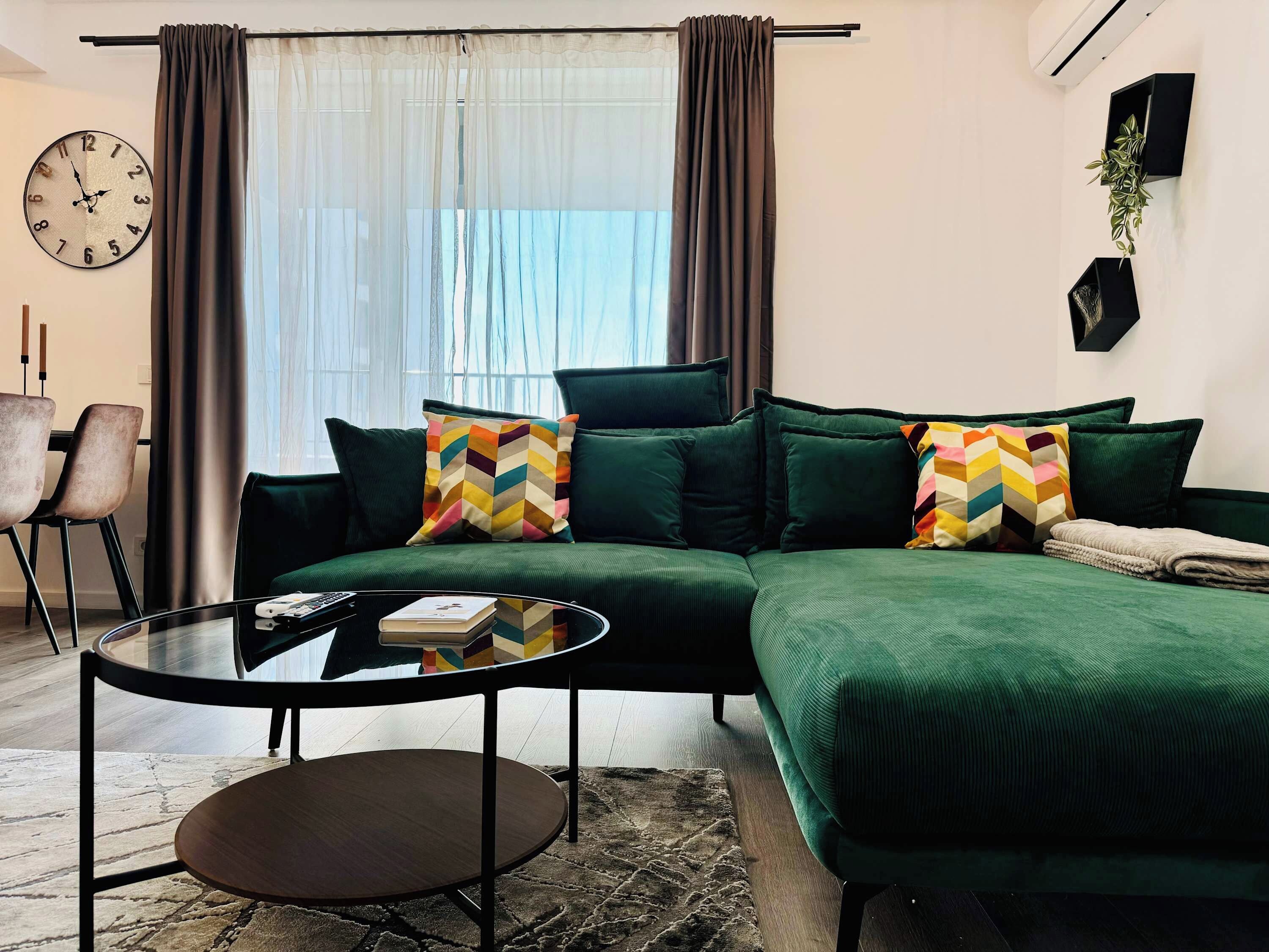 A modern living room with a green sofa, a round coffee table, and a large window with curtains.