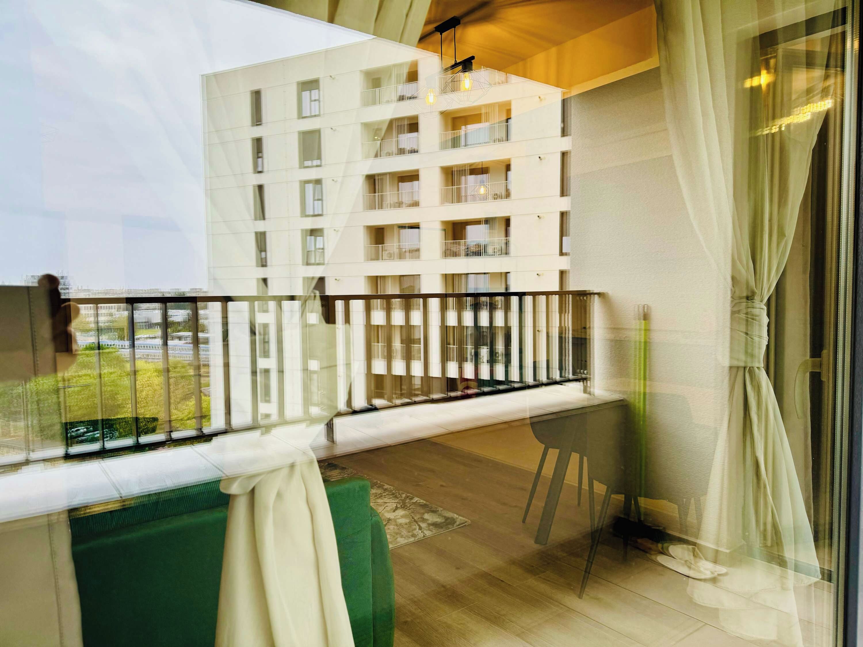A balcony with a view of a modern building, a glass door, and a green cushion.