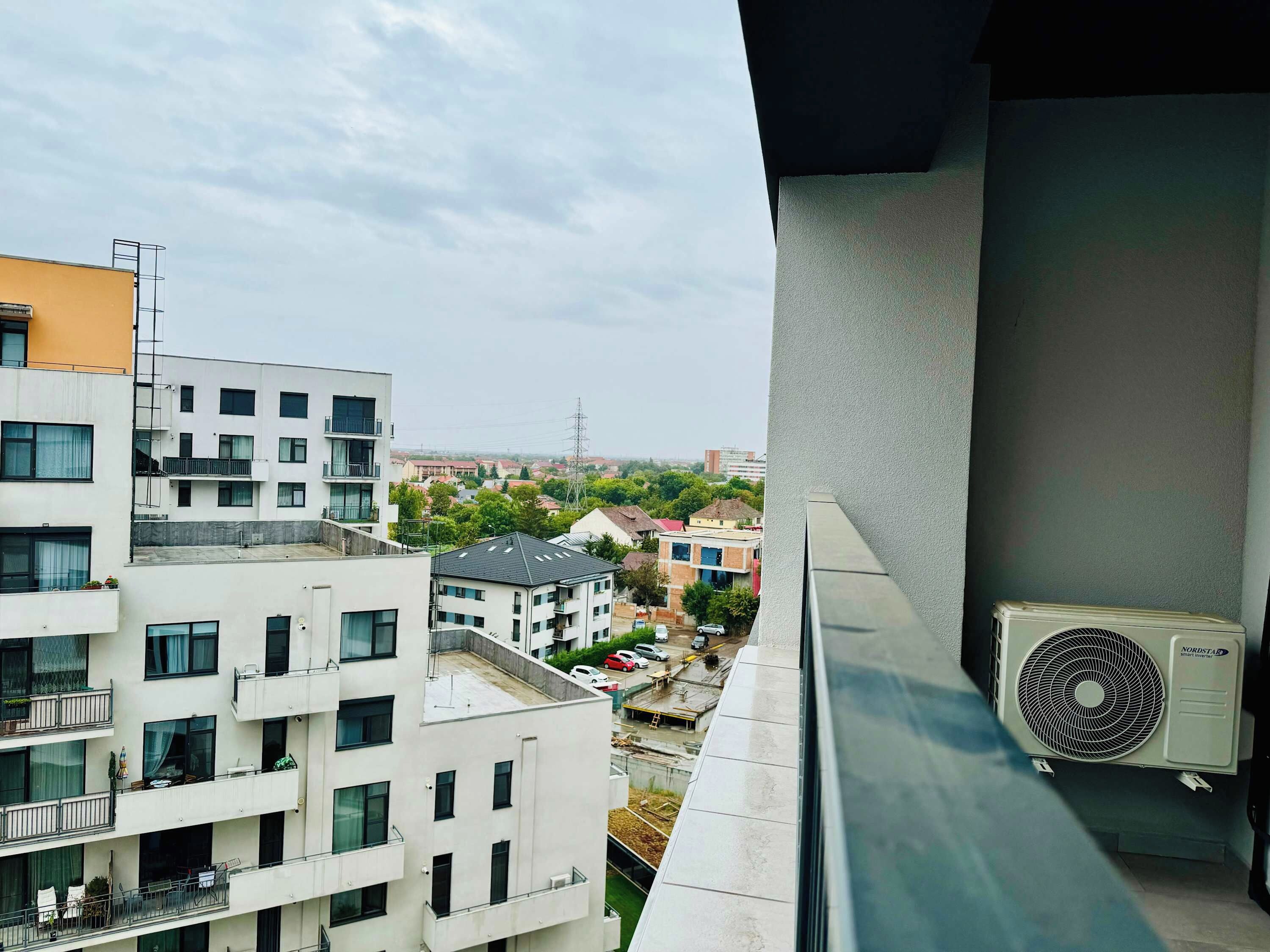 Um edifício alto com várias varandas, um aparelho de ar condicionado visível e vista para edifícios residenciais ao redor.