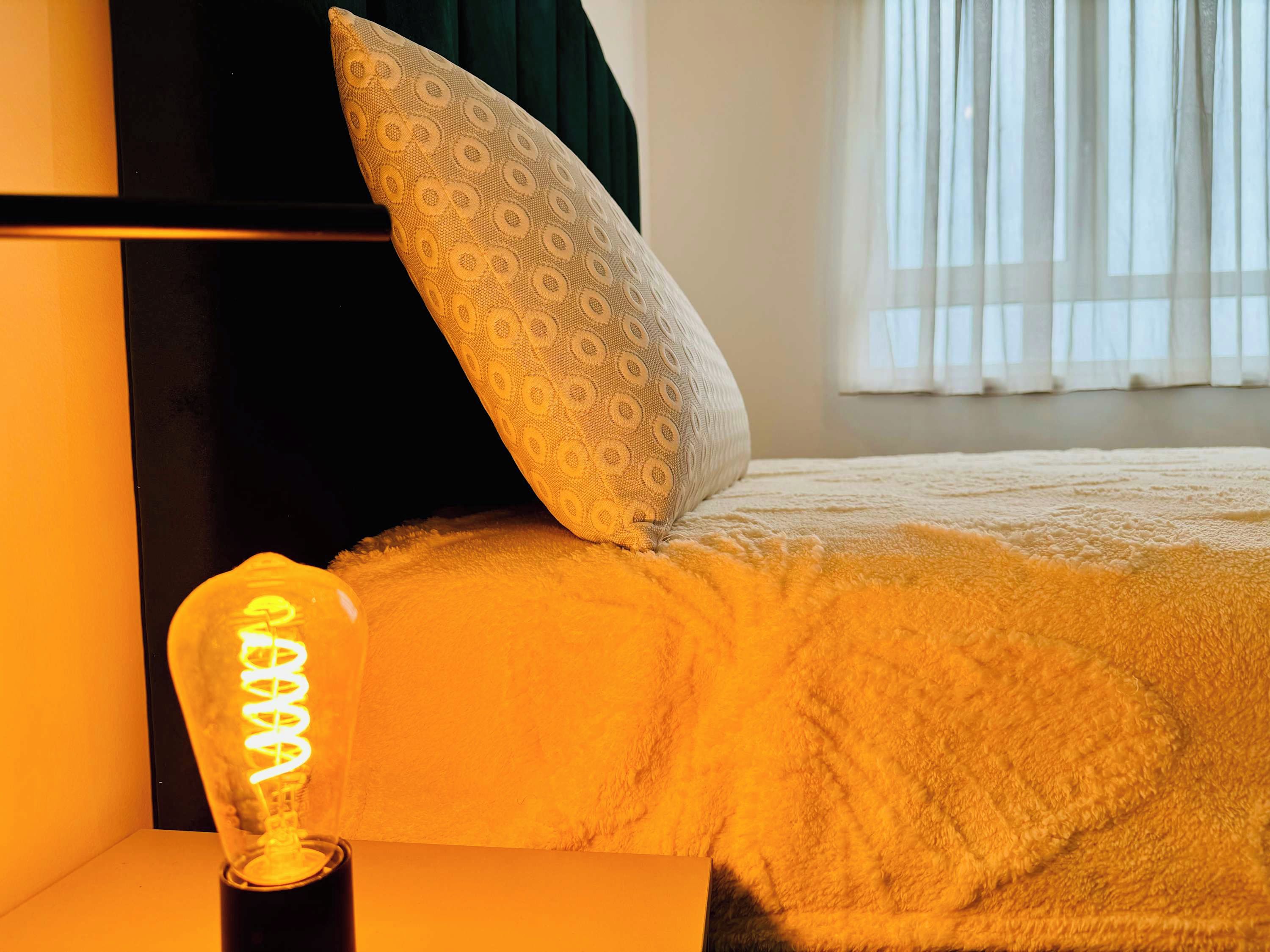 Ein Bett mit einem gemusterten Kopfkissen und einer Leuchte an der Kopfteil.