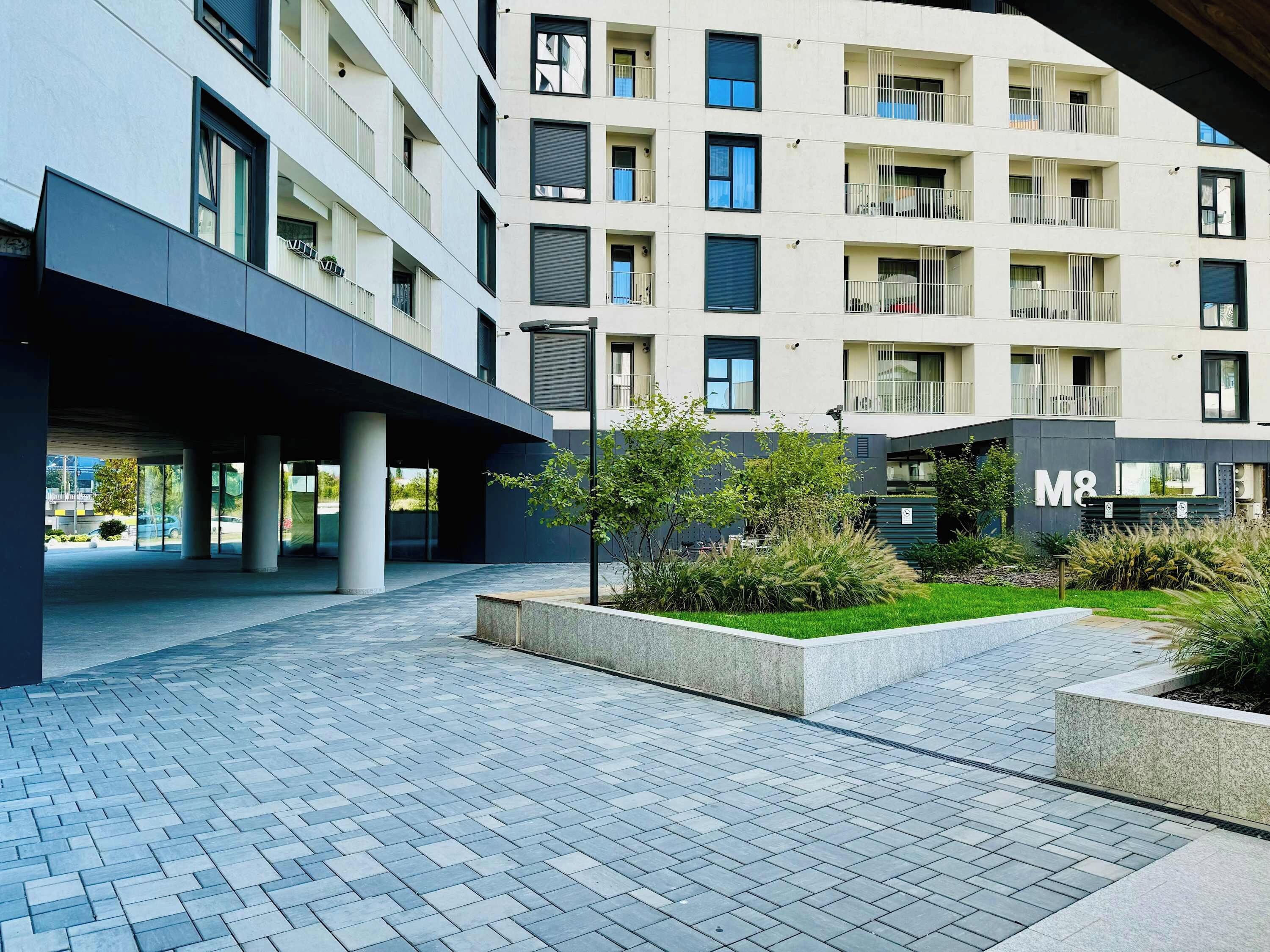 A modern building with multiple balconies and a paved courtyard.