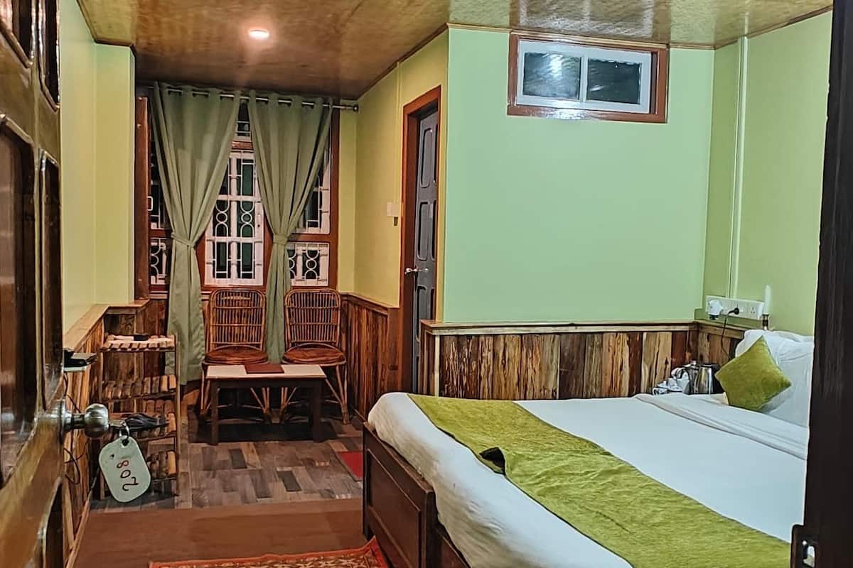 A bedroom with a large bed, a wooden headboard, a green throw, and a patterned rug.