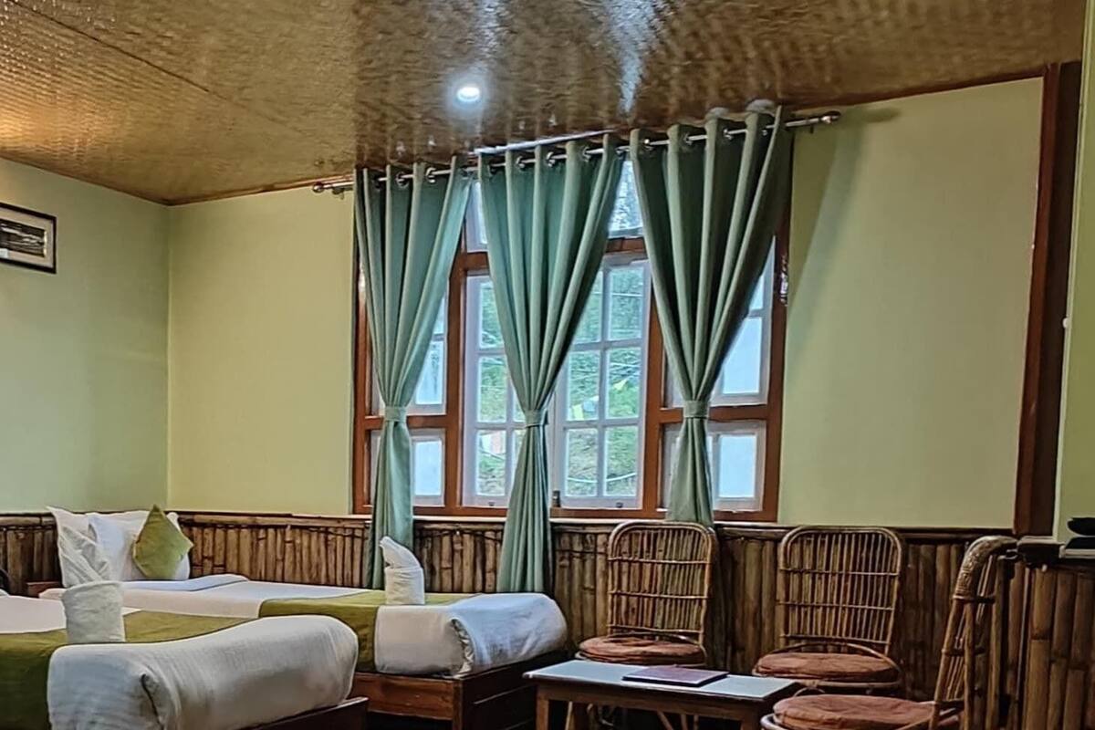 A room with a wooden ceiling, green curtains, a bed, a table, and wicker chairs.