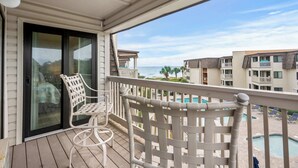 A balcony with a white chair and a table, overlooking a swimming pool and a beach. - Ocean Forest Villas D314 - Ocean View! (Myrtle Beach)