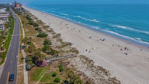 An aerial view of a beach with a road running parallel to it, a pedestrian bridge, and buildings in the background. - Ocean Forest Villas D314 - Ocean View! (Myrtle Beach)
