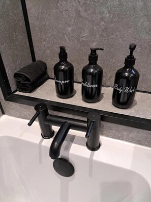 A bathroom with a black shelf holding three black bottles labeled "Shampoo," "Conditioner," and "Body Wash." - Renfrew Apartment Near Glasgow Airport (Renfrew)