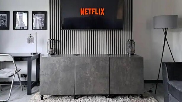A modern living room with a large flat-screen TV mounted on a wall, a grey entertainment unit below, and a minimalist design with a striped wall panel. - Renfrew Apartment Near Glasgow Airport (Renfrew)
