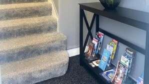 A carpeted staircase with a welcome sign, a vase with flowers, and a console table with magazines. - Renfrew Apartment Near Glasgow Airport (Renfrew)