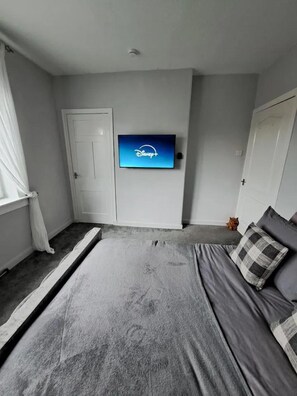 A bedroom with a bed, a television mounted on the wall, and a door. - Renfrew Apartment Near Glasgow Airport (Renfrew)