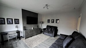 A modern living room with a grey sofa, a black TV, and a grey console table. - Renfrew Apartment Near Glasgow Airport (Renfrew)
