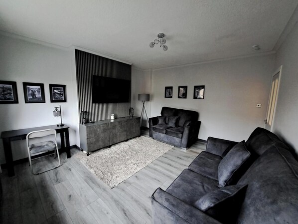 A modern living room with a grey sofa, a black TV, and a grey console table. - Renfrew Apartment Near Glasgow Airport (Renfrew)