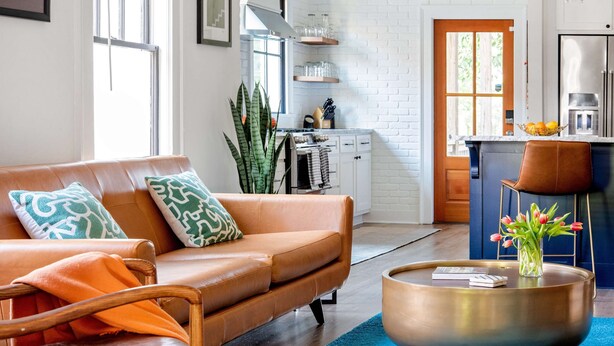 Una sala moderna con un sofá de cuero, una mesa de centro y una cocina al fondo.