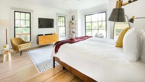 Un dormitorio amplio con una cama grande, un ventilador de techo, un televisor montado en la pared y vistas a zonas verdes.
