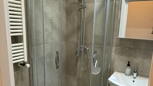 Eine Dusche mit Glasabtrennung, ein weißes Waschbecken und ein Spiegel darüber.