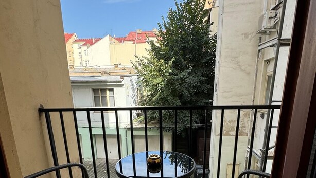 Ein kleiner Balkon mit rundem Tisch und zwei Stühlen, einem Blumentopf und Blick auf Gebäude im Hintergrund.