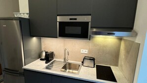 Eine moderne Küche mit dunklen Schränken, einem Edelstahlkühlschrank, einem Einbauofen, einer Mikrowelle, einem Spülbecken und einem Toaster.