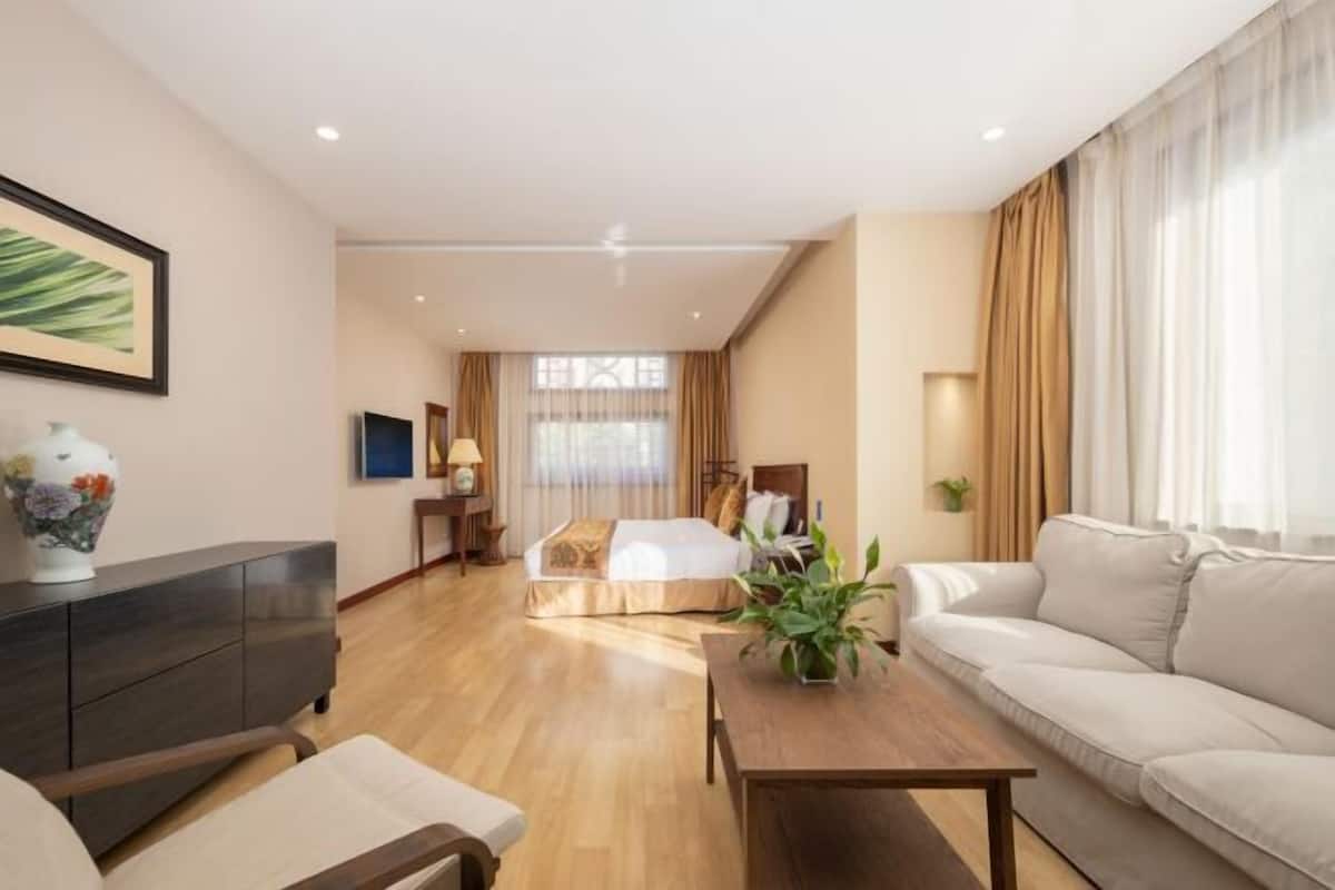 A hotel room with a bed, a sofa, a coffee table, a TV, and a window with curtains.