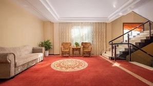 Una habitación con alfombra roja, un sofá, dos sillones, una mesita con una planta y una escalera con barandilla de vidrio.
