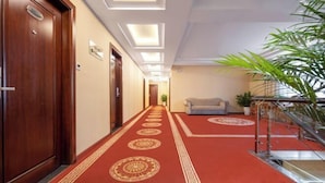 Un pasillo de hotel con alfombra roja, puertas de madera y una escalera con barandilla de cristal.
