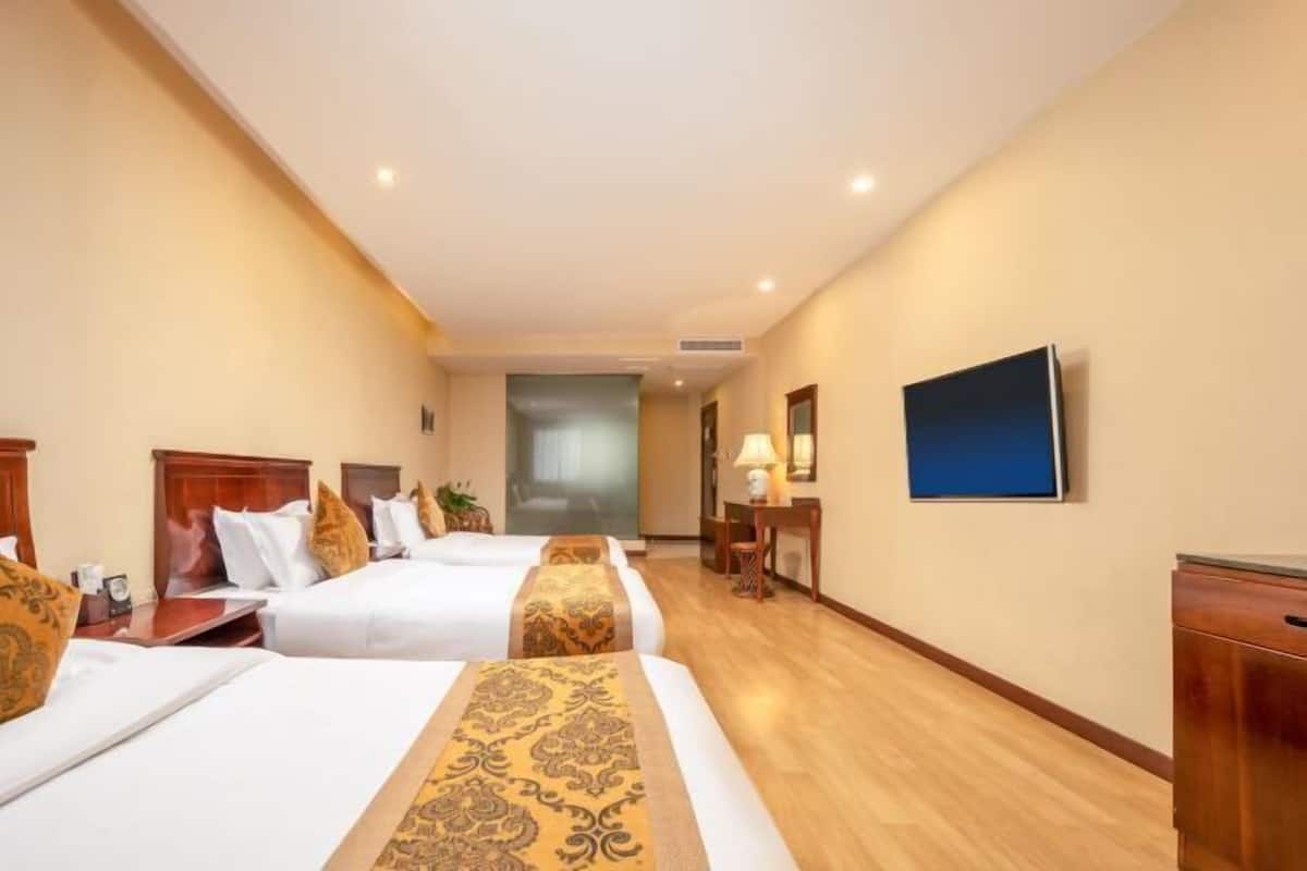 A hotel room with three beds, a TV, a desk, and a lamp.