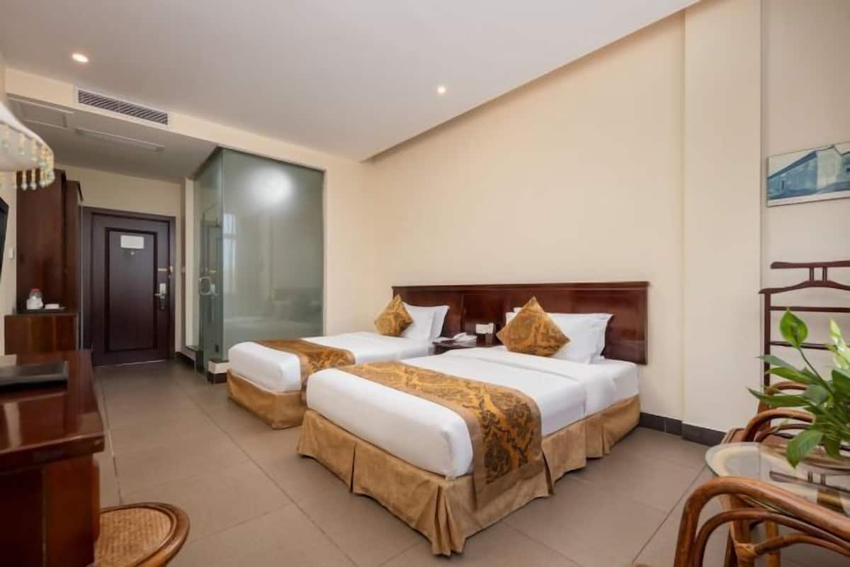 A hotel room with two beds, a desk, a chair, and a glass shower enclosure.