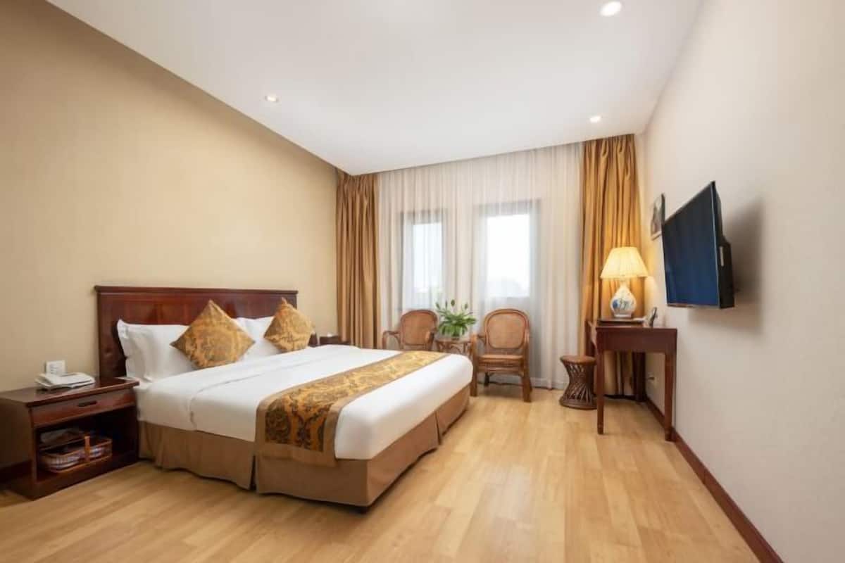 A hotel room with a large bed, a TV, a desk, and a chair.