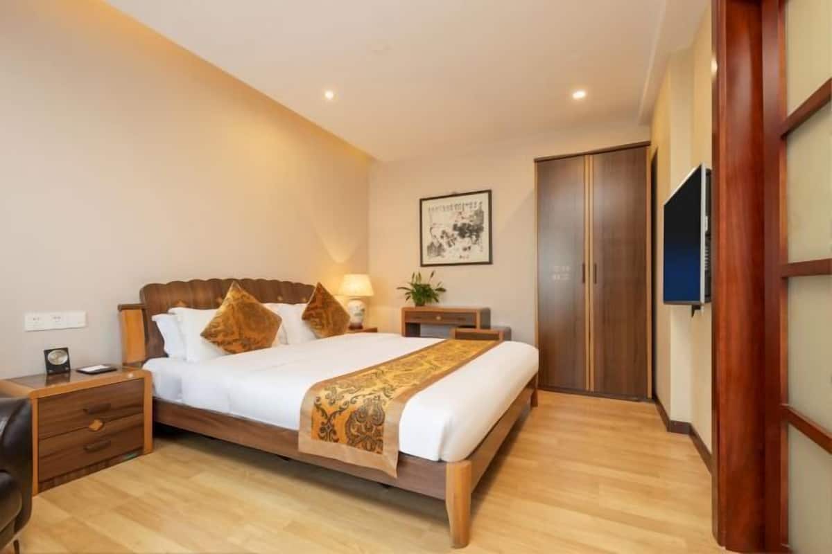 A hotel room with a wooden bed, bedside tables, a TV, a wardrobe, and a framed picture on the wall.