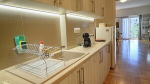 A kitchen with wooden cabinets, a sink, a coffee maker, and a dish rack. - Lecabetus view apartment (Athina)