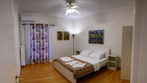 A bedroom with a bed, a ceiling fan, a nightstand, a lamp, and a painting on the wall. - Lecabetus view apartment (Athina)