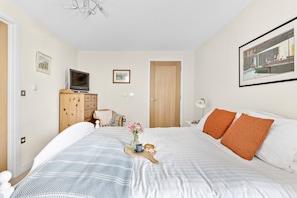 A bedroom with a bed, a wooden dresser, a television, and a framed picture on the wall.