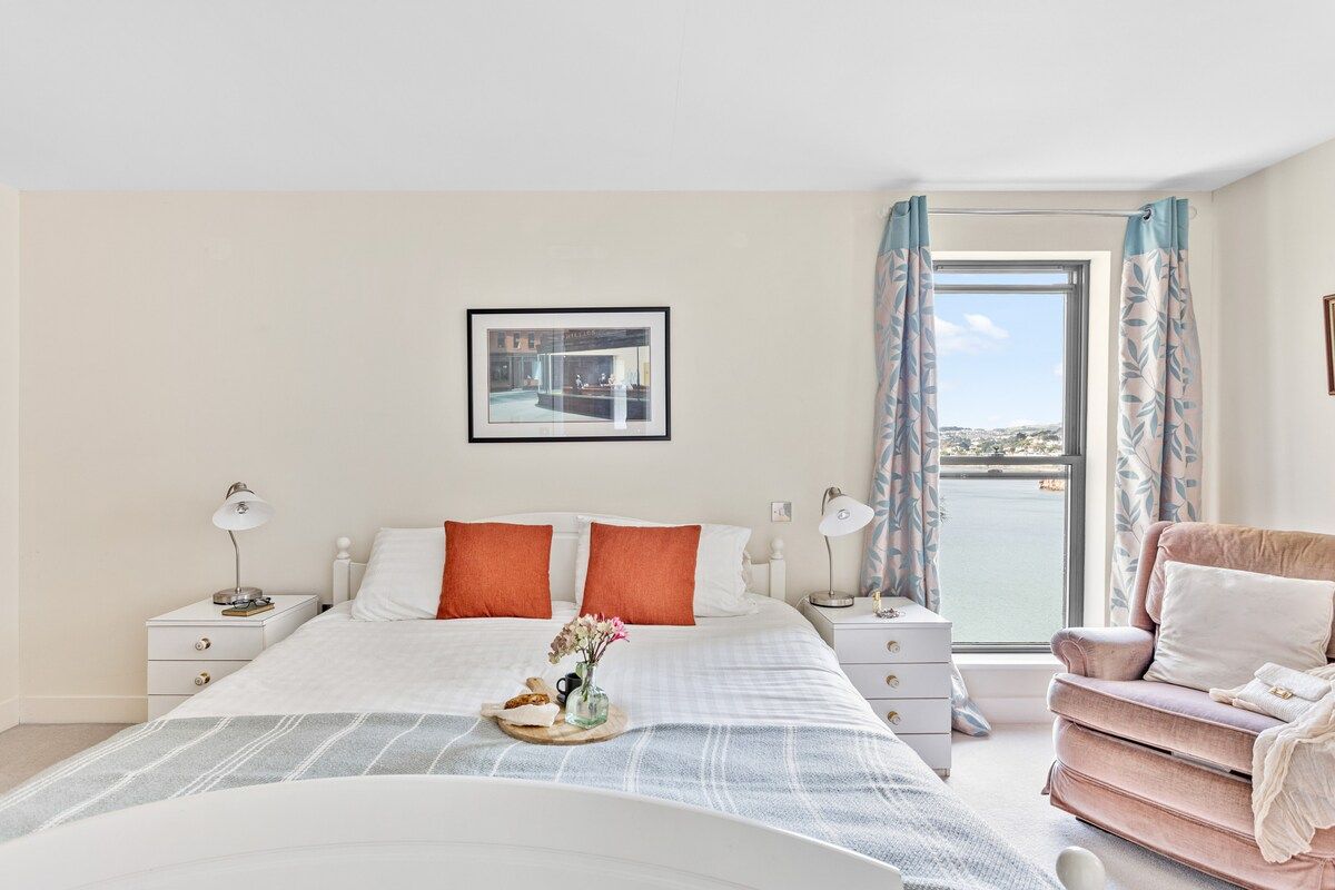 A hotel room with a bed, bedside tables, a window with a view, and a chair.