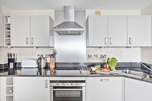 A modern kitchen with white cabinets, a stainless steel range hood, a built-in oven, and a granite countertop.