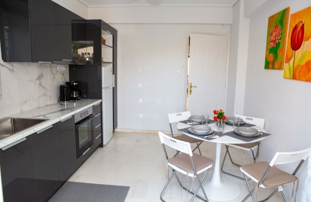 A compact kitchen with modern appliances, a dining area with a white table and chairs, and a door leading to another room.
