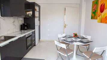 A compact kitchen with modern appliances, a dining area with a white table and chairs, and a door leading to another room.