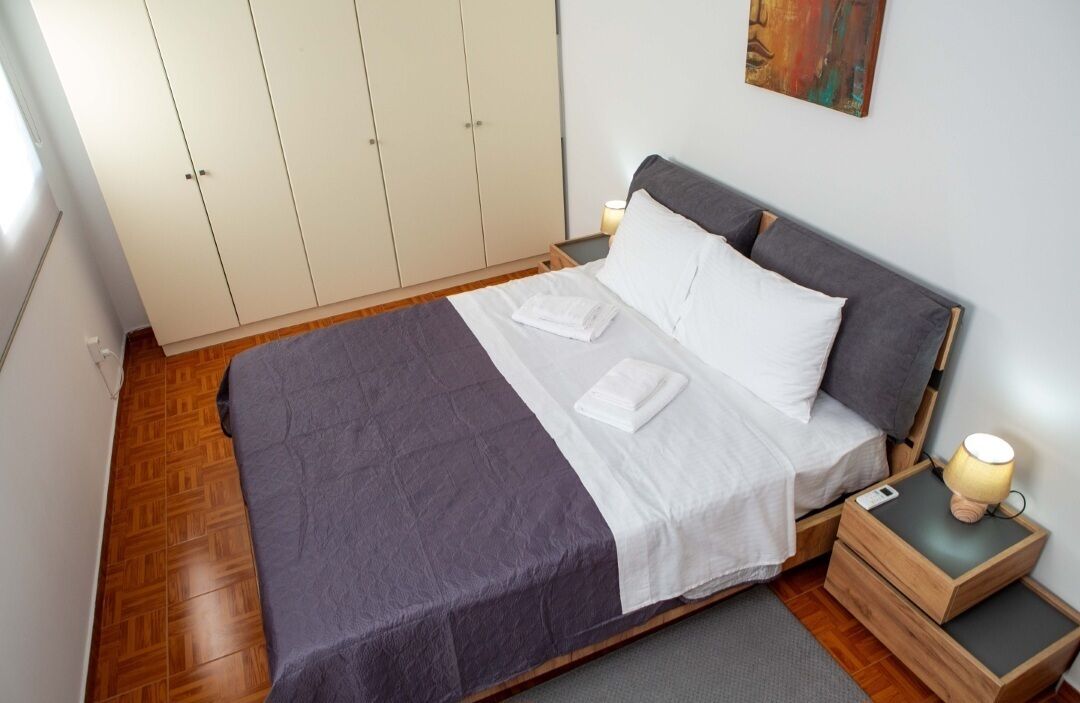 A neatly made bed with a grey and white duvet, a wooden nightstand with a lamp, and a wardrobe with a light-colored finish.