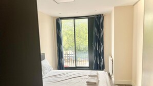 Et hotelværelse med seng, et vindue med gardiner, en radiator og en balkon med gelænder.