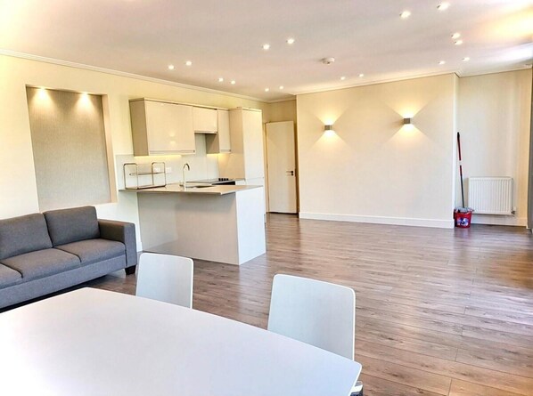 A modern, well-lit living area with a sofa, a dining table, and a kitchen island. - London Riverside Apartment Retreat (London)