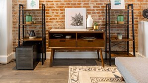 Ein Zimmer mit Backsteinwand, einem Holztisch mit Regalen, einem kleinen schwarzen Gerät und einem gemusterten Teppich.