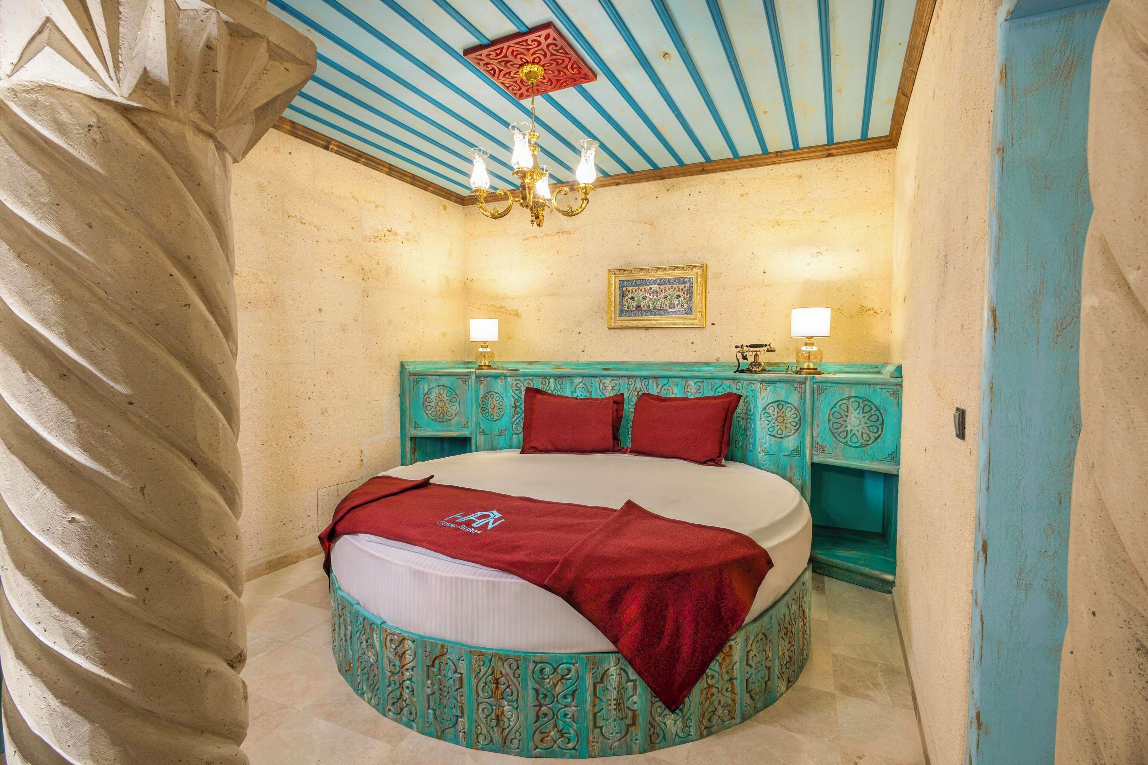 Un letto rotondo con una coperta rossa, una testiera turchese e un lampadario.