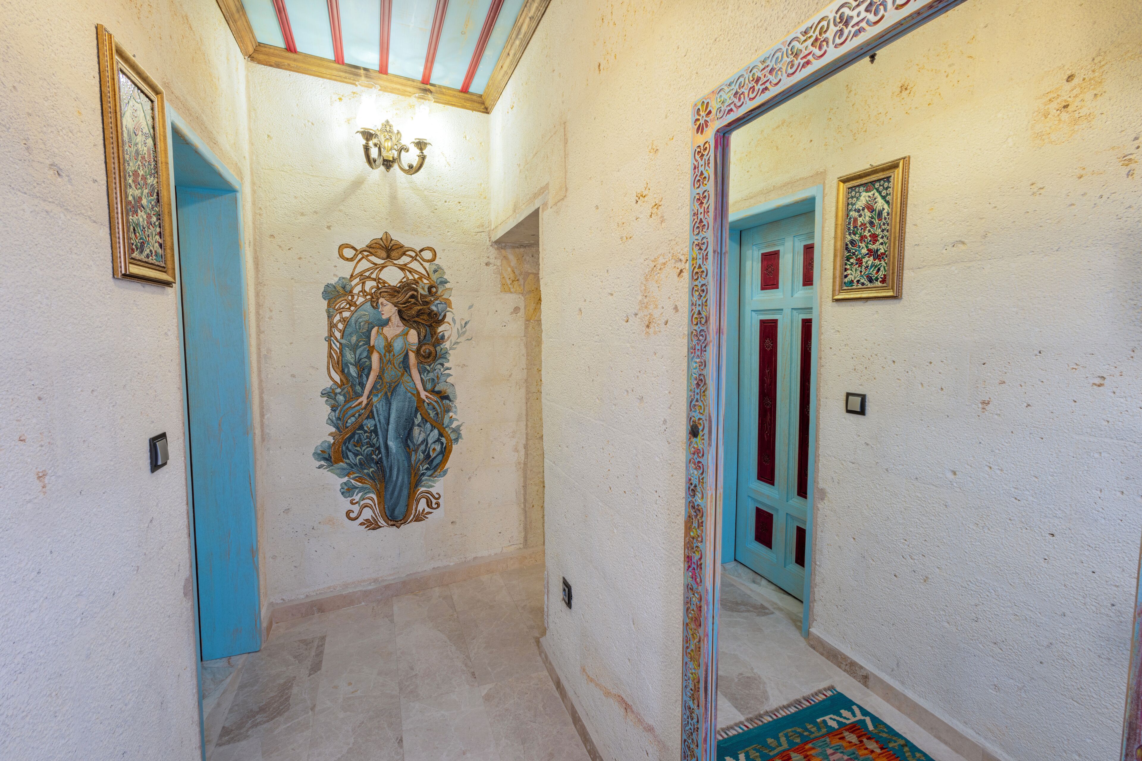 A hallway with a blue door, a decorative wall mural, and a mirror reflecting the door.