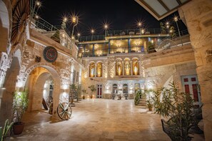 A historic building with stone arches, a courtyard with potted plants, and a large wheel. - Han Cave Suites - The Special class (Nevsehir)
