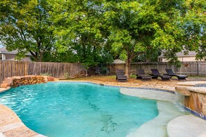 Un jardin avec une piscine, des chaises longues et une clôture en bois.