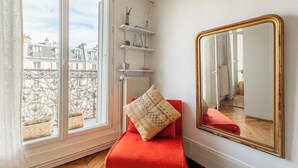 A room with a red chair, a large mirror, and a window overlooking a balcony with plants.