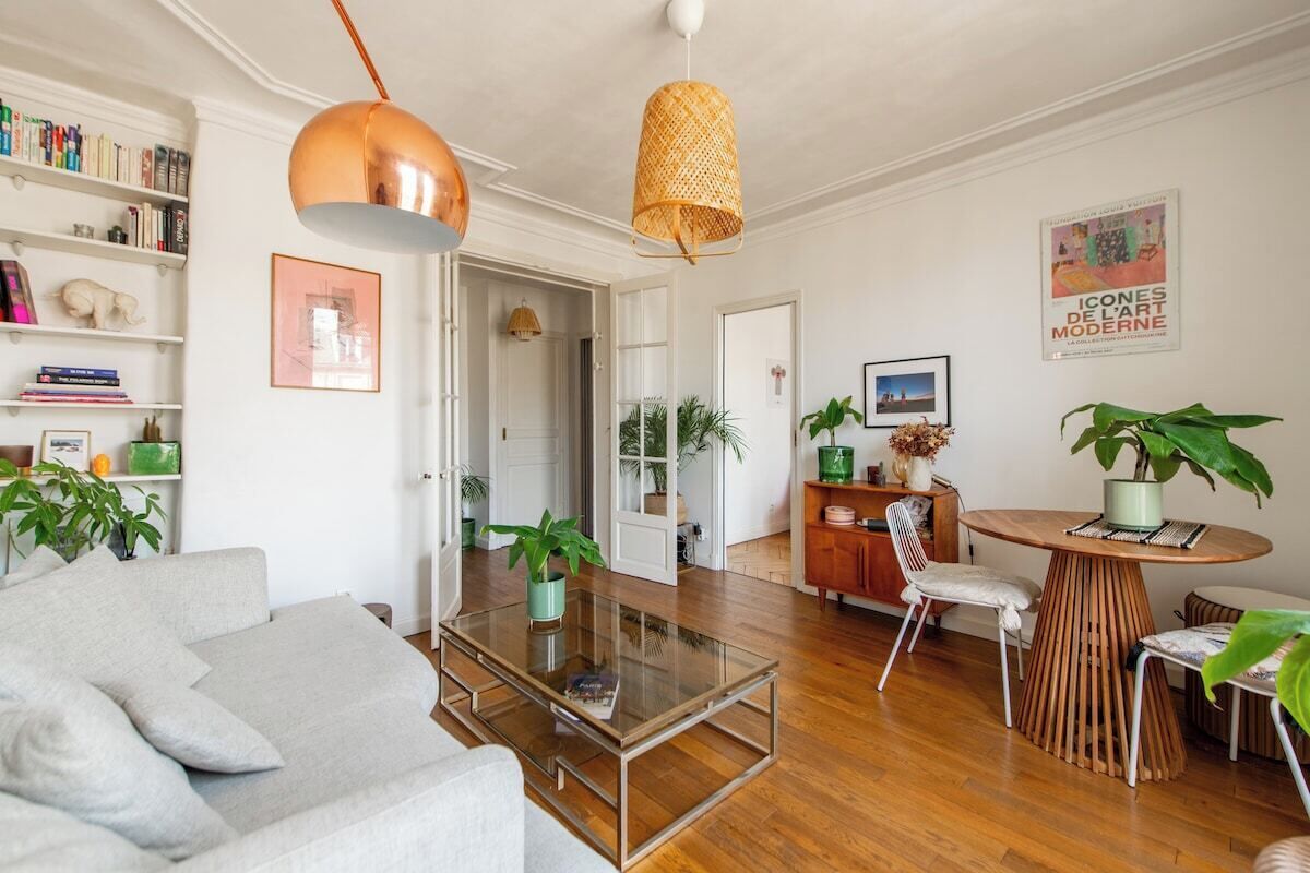 A modern living room with a glass coffee table, a grey sofa, wooden flooring, and a dining area with a round table and chairs.